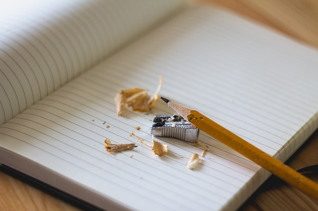 Empty notebook opened up with a pencil leaning on top of it with a sharpener and shavings